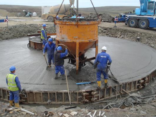 Arbeiter füllen Beton aus einer Betonbombe in eine Windkraftturm Fundament, Im Hintergrund der Betonmischer CARMIX 5.5XL